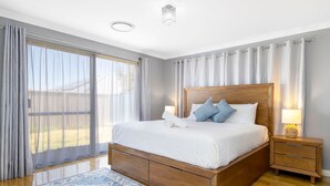 Une chambre à coucher avec un lit en bois, deux tables de chevet, une lampe de chevet et des rideaux légers.