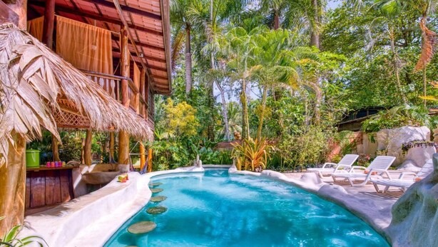 A swimming pool with lounge chairs and a thatched-roof structure. - Caribe Town Bungalows (Cahuita)