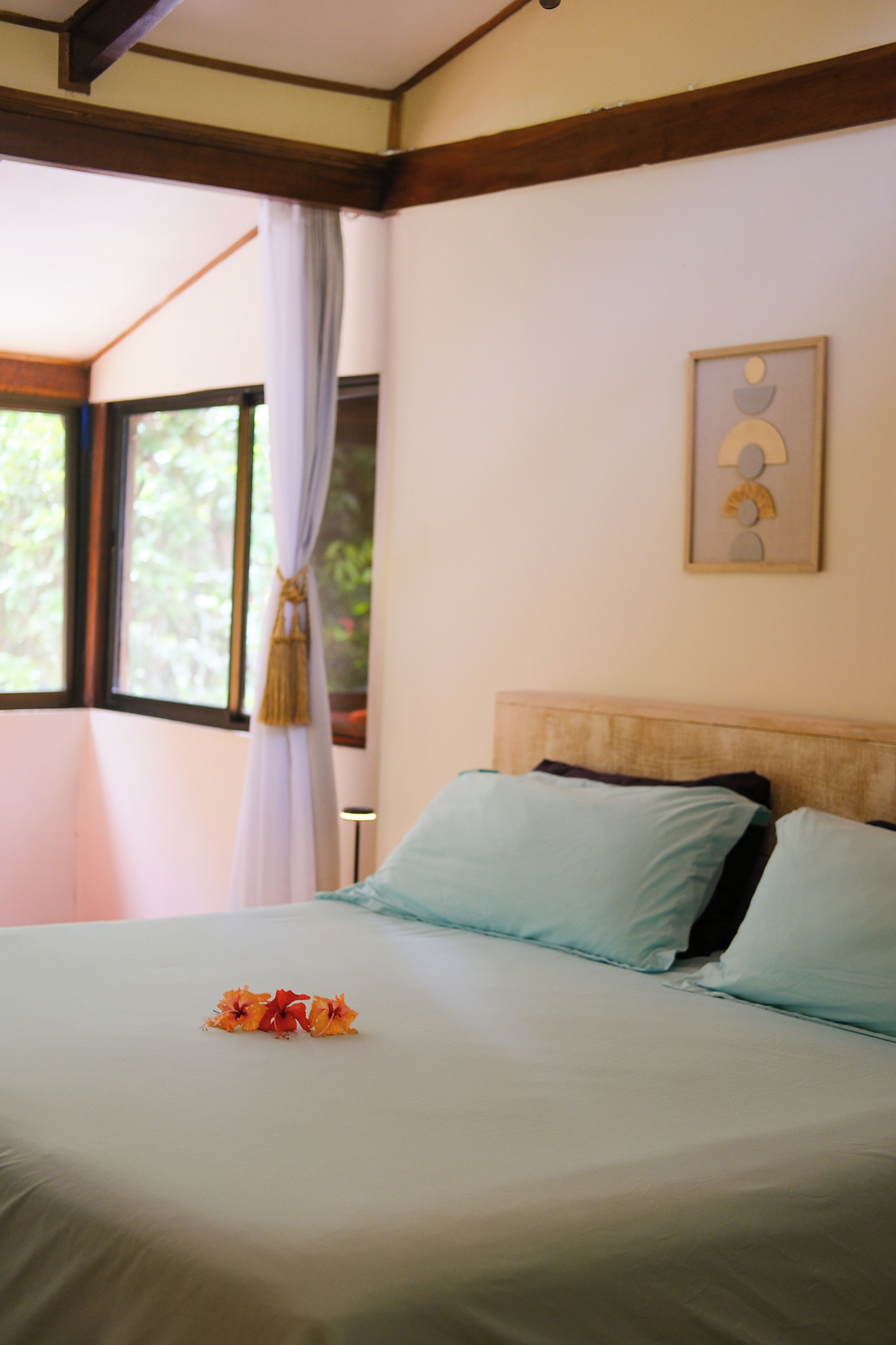 Una cama con cabecera, un ventanal con cortinas y una obra de arte colgada en la pared.