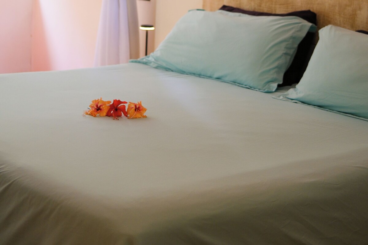 A bed with a headboard, a window with curtains, and a wall-mounted artwork.