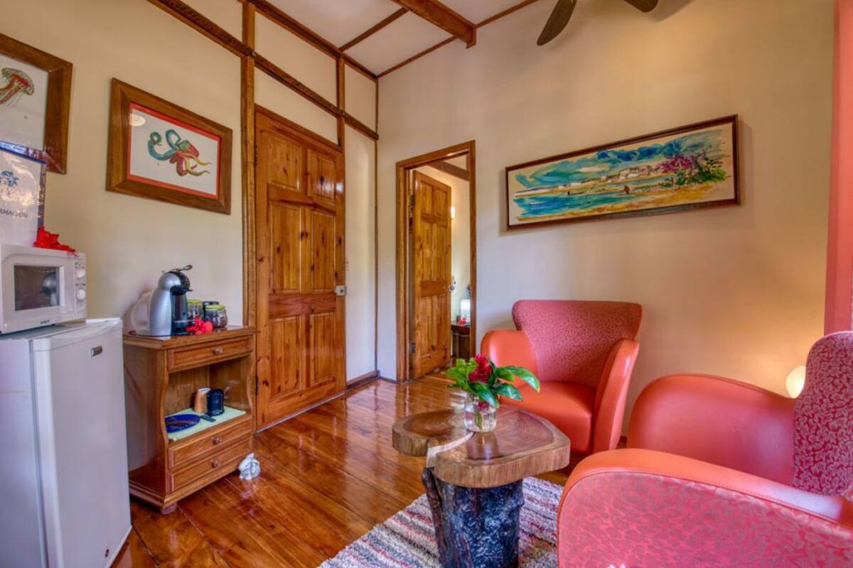 Una sala de estar con suelo de madera, un sillón rojo, una mesa de centro con un jarrón y un cuadro de una playa.