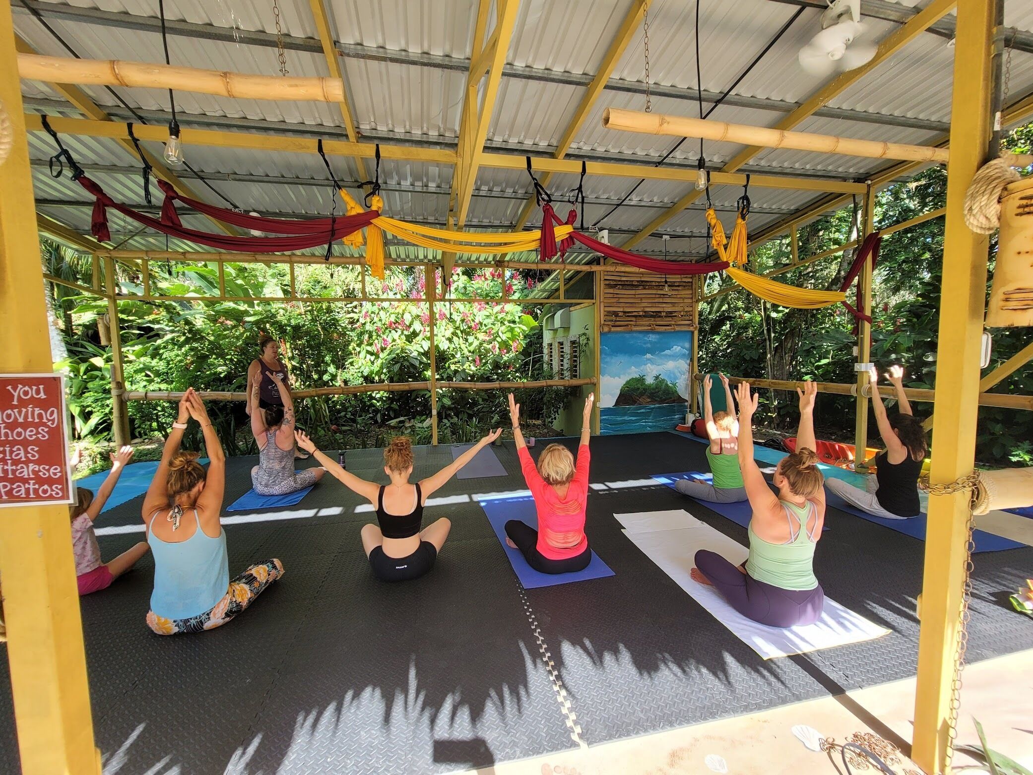 Un grupo de personas practicando yoga sobre esterillas en un espacio cubierto con un mural de paisaje tropical.