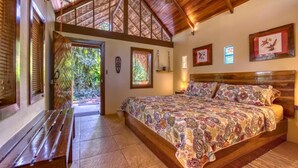 A bedroom with a wooden bed, a bench, and a view of the outdoors. - Caribe Town Bungalows (Cahuita)