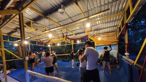 An indoor training facility with a boxing ring, mats, and a ceiling with exposed beams and lighting fixtures. - Caribe Town Bungalows (Cahuita)