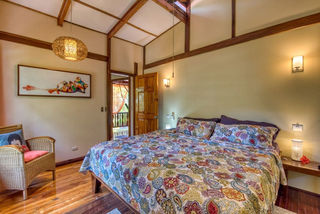 Un dormitorio con una cama grande, una silla de mimbre, una puerta de madera y un cuadro en la pared.