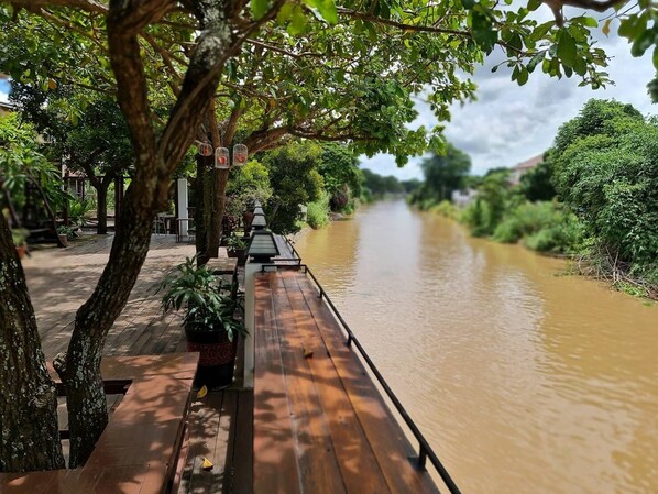 A riverside walkway with wooden benches and potted plants, surrounded by lush greenery and trees. - Romyen cafe homestay (Ayutthaya)