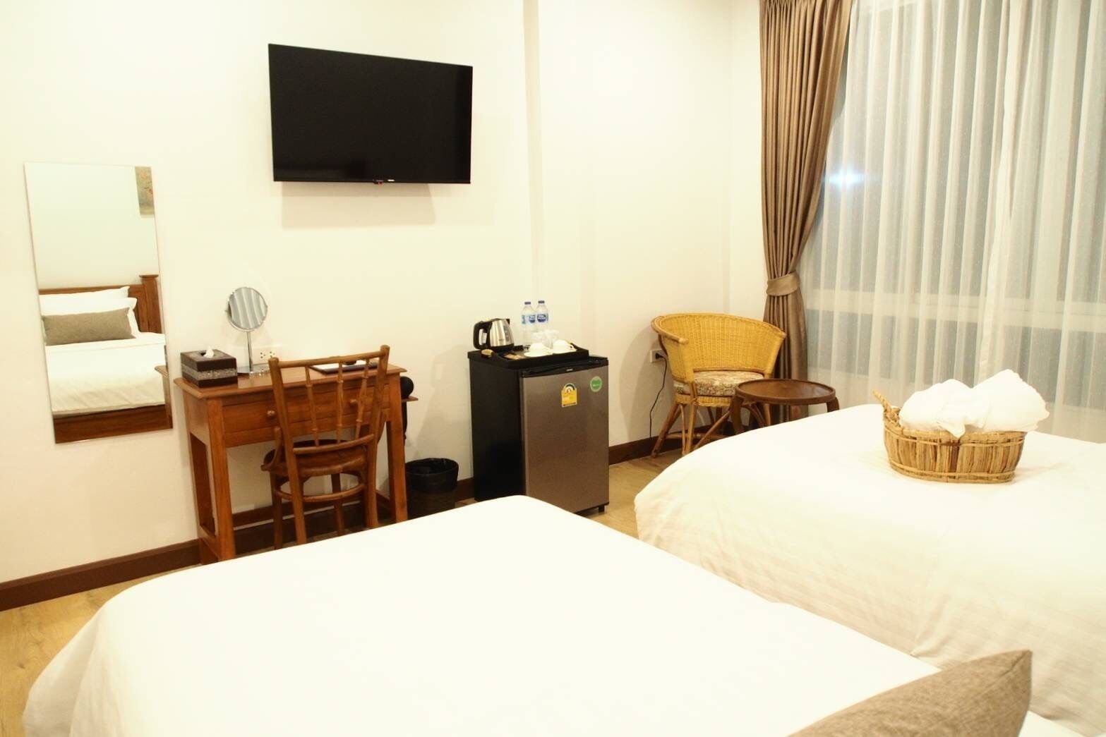 A hotel room with two beds, a desk with a chair, a television, a small refrigerator, and a wicker basket on the bed.