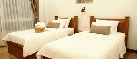A hotel room with two wooden beds, white bedding, a wicker basket on one bed, and a floral painting on the wall.