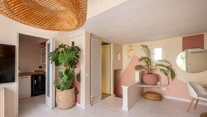A spacious living area with a large potted plant, a wicker ceiling light, and a modern kitchen in the background. - ARIA - Penthouse & Garden (Roma)