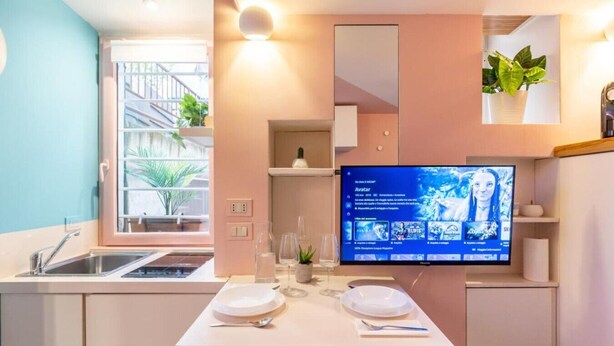 A modern kitchen with a built-in TV, a sink, and a dining area with a white table set for two. - Romantic Rome Retreat, Steps from Colosseum (Roma)