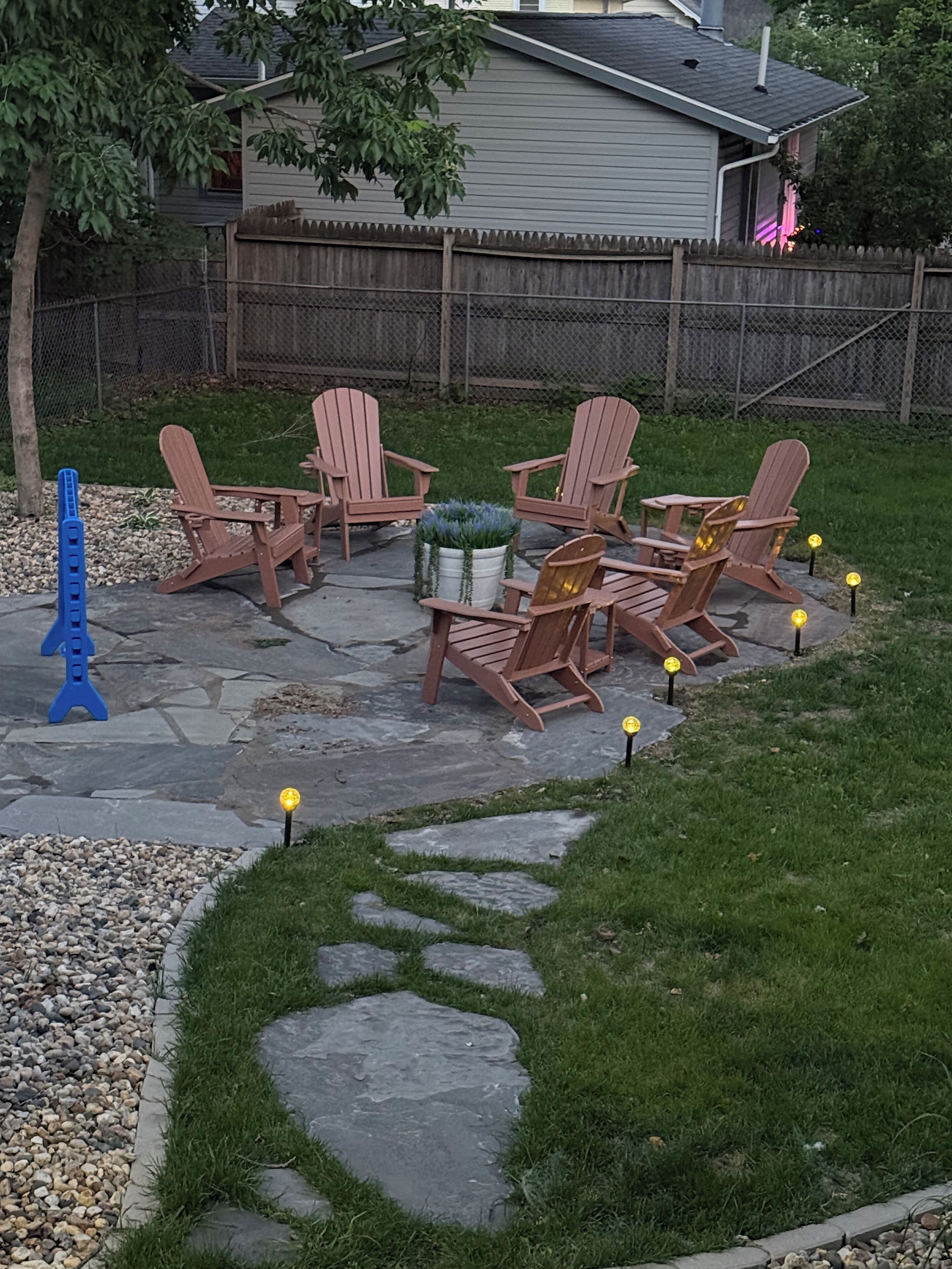 Un patio trasero con sillas Adirondack, una escultura azul y una planta en maceta.