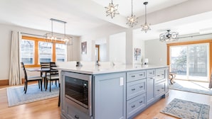 A modern kitchen with a large island, built-in oven, and a dining area with chairs and a table.