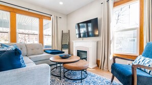 A living room with a sofa, armchair, and ottoman, a fireplace, and a TV mounted on the wall.