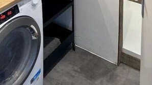 Ein modernes Badezimmer mit Waschmaschine, Waschbecken und einem schwarzen Wasserhahn sowie einem großen Spiegel über dem Waschbecken.