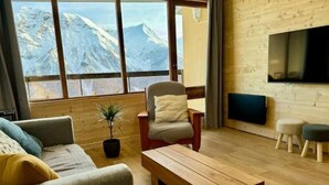 Ein gemütliches Wohnzimmer mit Holzboden, einer Couch, einem Sessel, einem Couchtisch und einem Fernseher.