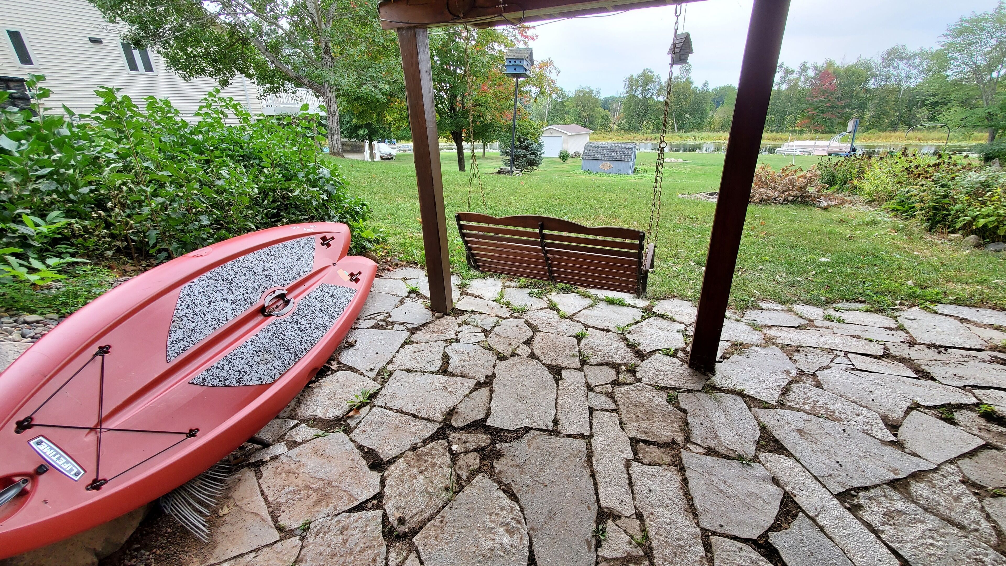 Une terrasse en pierre avec une balançoire et un kayak rouge.