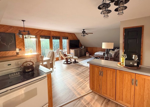 A modern kitchen with a stove, wooden cabinets, and a dining area with a chair.
