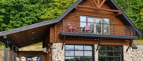 Eine Blockhütte mit Steinfundament, einer großen Garagentür und einer überdachten Terrasse mit Sitzgelegenheit im Freien.