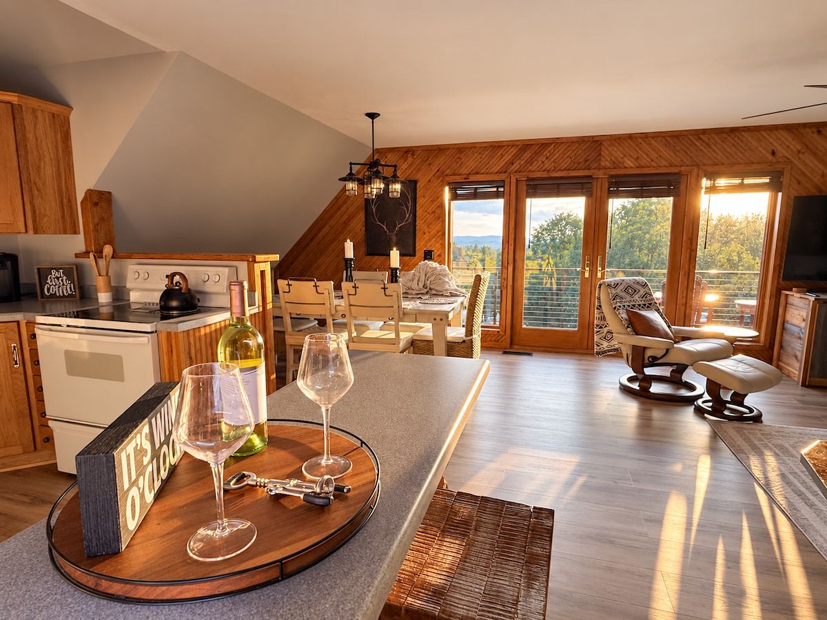 A modern kitchen with a dining area, wooden flooring, and large windows.
