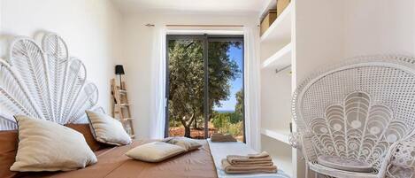 Un dormitorio con cama, una silla, vistas a árboles y una puerta que da al exterior.