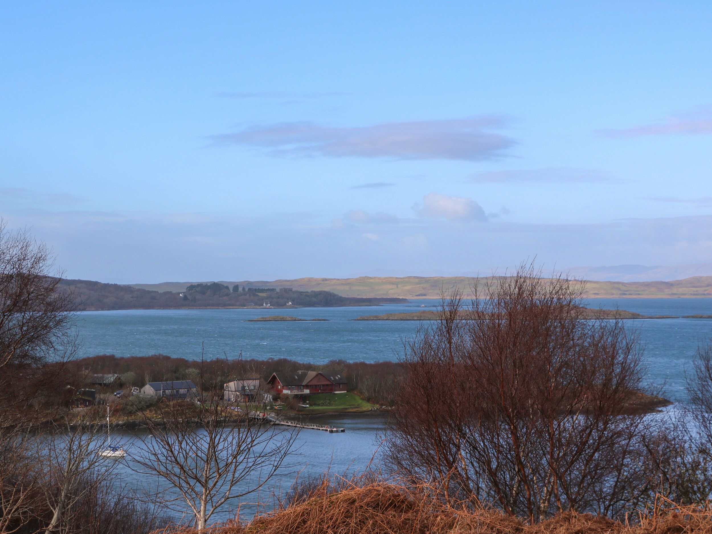 A coastal landscape with a body of water, a small island with buildings, and distant hills.