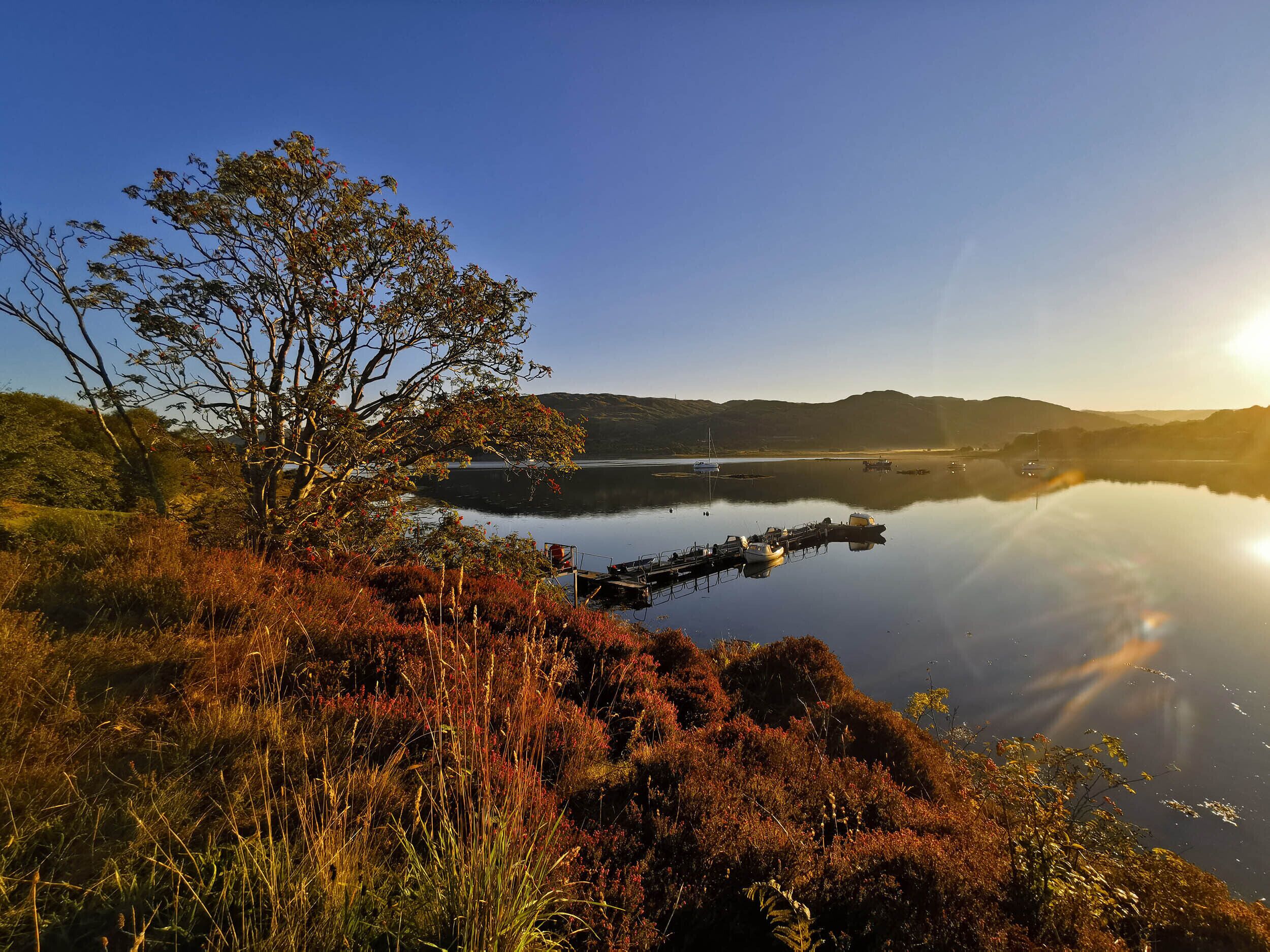 A calm lake with boats docked, surrounded by hills and autumn foliage.
