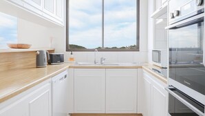 A modern kitchen with white cabinetry, a wooden countertop, a double sink, and a large window providing a view of the sky. - Royal Palms Uninterrupted Views (Palm Beach)