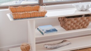 A room with a large window overlooking a beach and ocean. There is a white shelf with a woven basket, a book, and a decorative item. - Royal Palms Uninterrupted Views (Palm Beach)