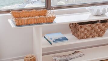 A room with a large window overlooking a beach and ocean. There is a white shelf with a woven basket, a book, and a decorative item.