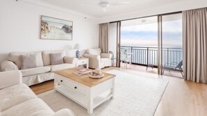 A spacious living room with a large window overlooking the sea, a white sofa set, a coffee table, and a ceiling fan. - Royal Palms Uninterrupted Views (Palm Beach)
