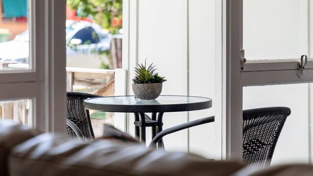 Et værelse med et rundt bord og to fletstole, en potteplante på bordet og udsigt ud gennem en dør.
