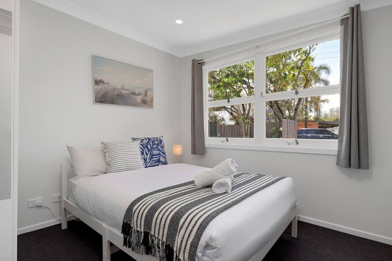 Une chambre à coucher avec un lit, une fenêtre avec des rideaux, un tableau au mur et une vue sur l’extérieur.