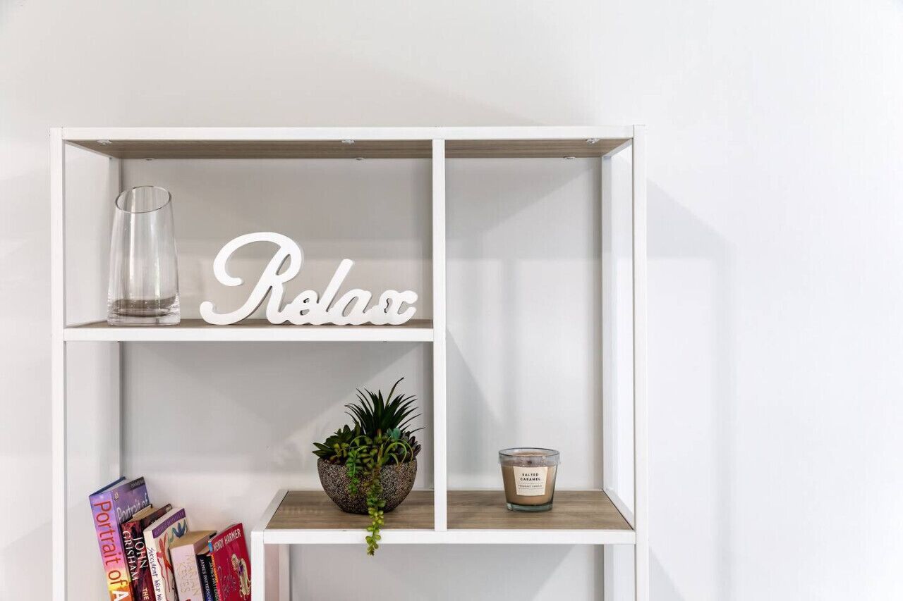 Een witte plank met een glas, een potplant, een kaars en boeken.