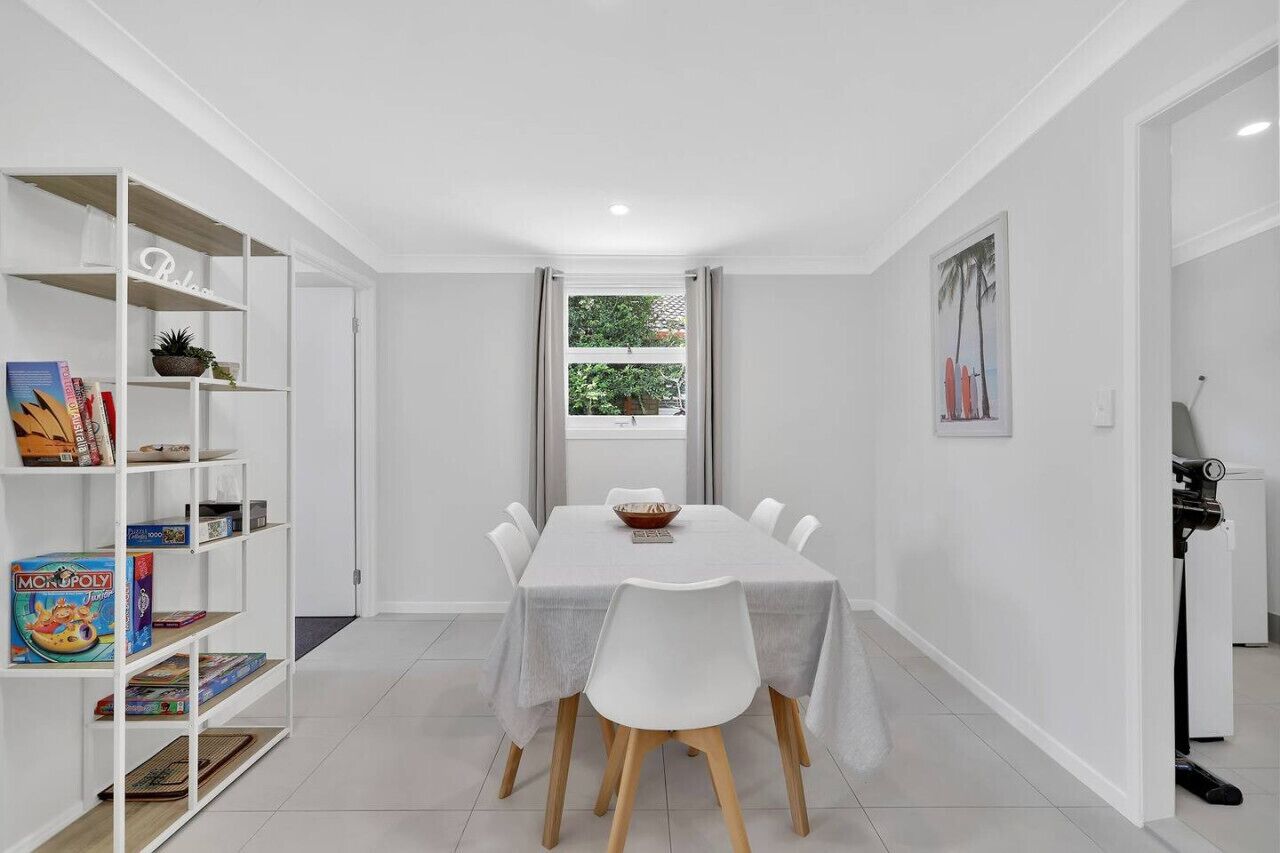 A dining area with a white table, chairs, and a bookshelf with books and board games.