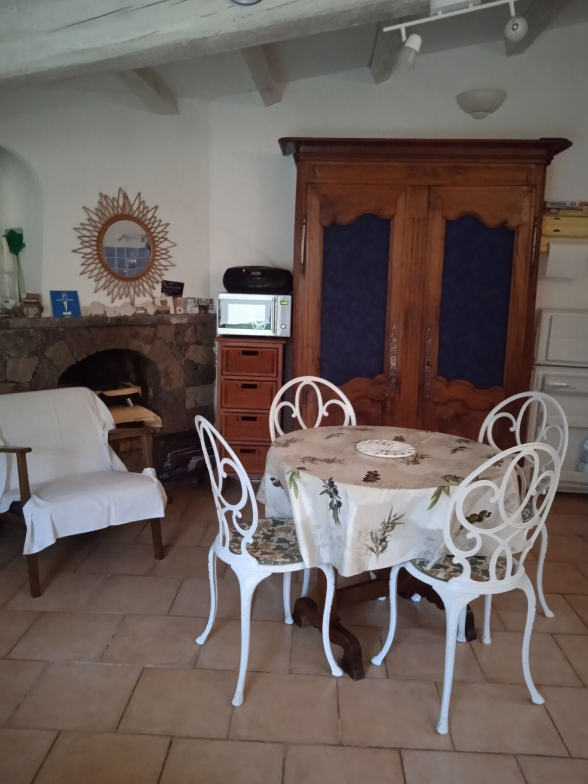 Un coin repas agrémenté d’une cheminée en pierre, de chaises blanches et d’une table recouverte d’une nappe à motifs floraux.