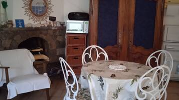 Un coin repas agrémenté d’une cheminée en pierre, de chaises blanches et d’une table recouverte d’une nappe à motifs floraux.