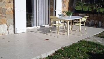 Un bâtiment en pierre doté d’une terrasse, d’une porte-fenêtre coulissante et d’une table avec des chaises.