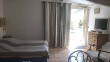Een slaapkamer met een bed, een televisie, een stoel en een raam met gordijnen.
