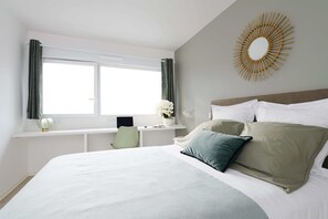 A bedroom with a large bed, a desk with a chair, a window with curtains, and a wall-mounted decorative item. - HOTEL LES PORTES DE PARIS (Ivry-sur-Seine)