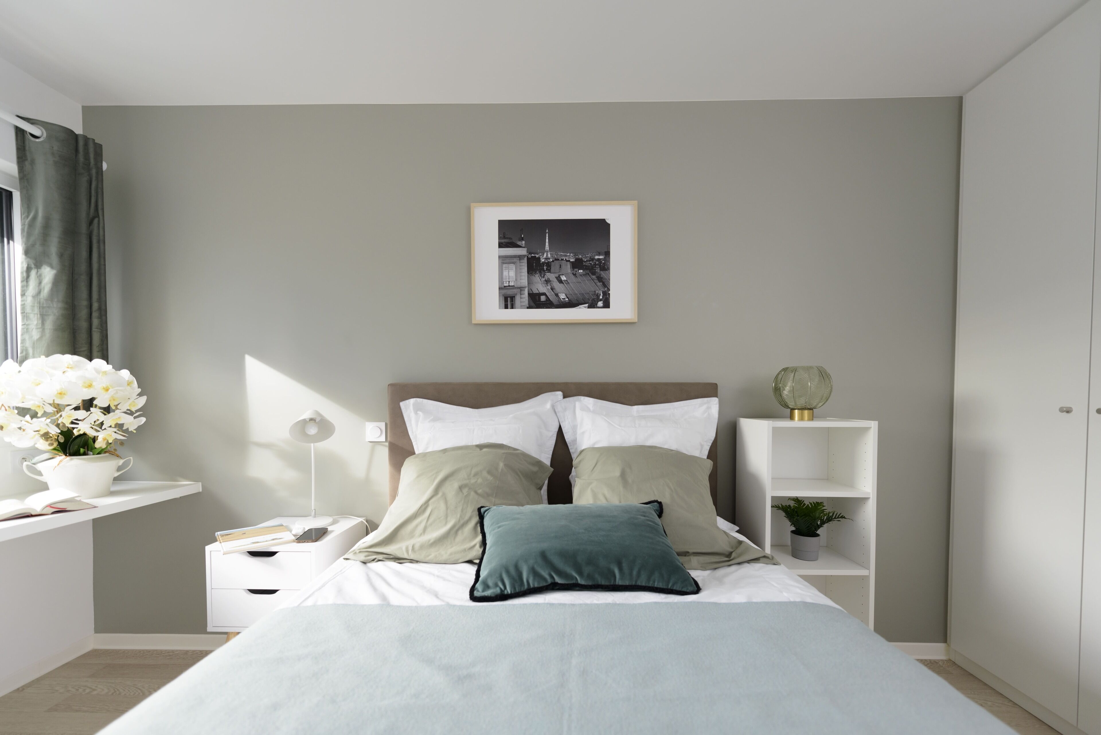 Une chambre à coucher moderne avec un lit, des tables de chevet, une commode, un tableau encadré au mur et une fenêtre avec des rideaux.