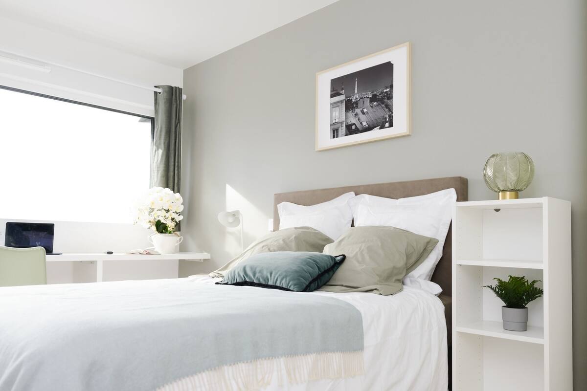 A modern bedroom with a bed, bedside tables, a desk, and a window.