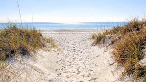 Ein sandiger Küstenpfad führt zum Meer, umgeben von Gras.