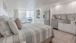 Ein modernes Schlafzimmer mit einem großen Bett, Meerblick und einer Küche mit weißen Schränken und Edelstahlgeräten.