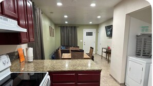 Eine Küche mit Granit Arbeitsplatten, roten Schränken, einem eingebauten Backofen und einem Essbereich mit Korbstühlen und einem Tisch.