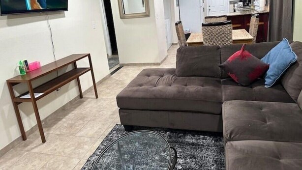 Ein Wohnzimmer mit Sofa, Couchtisch und Fernseher. Im Hintergrund befindet sich eine Küchenzeile.