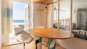 A room with a wooden table, white chair, and a view of the beach. - Old Saltings, overlooking Porthmeor beach (St Ives)