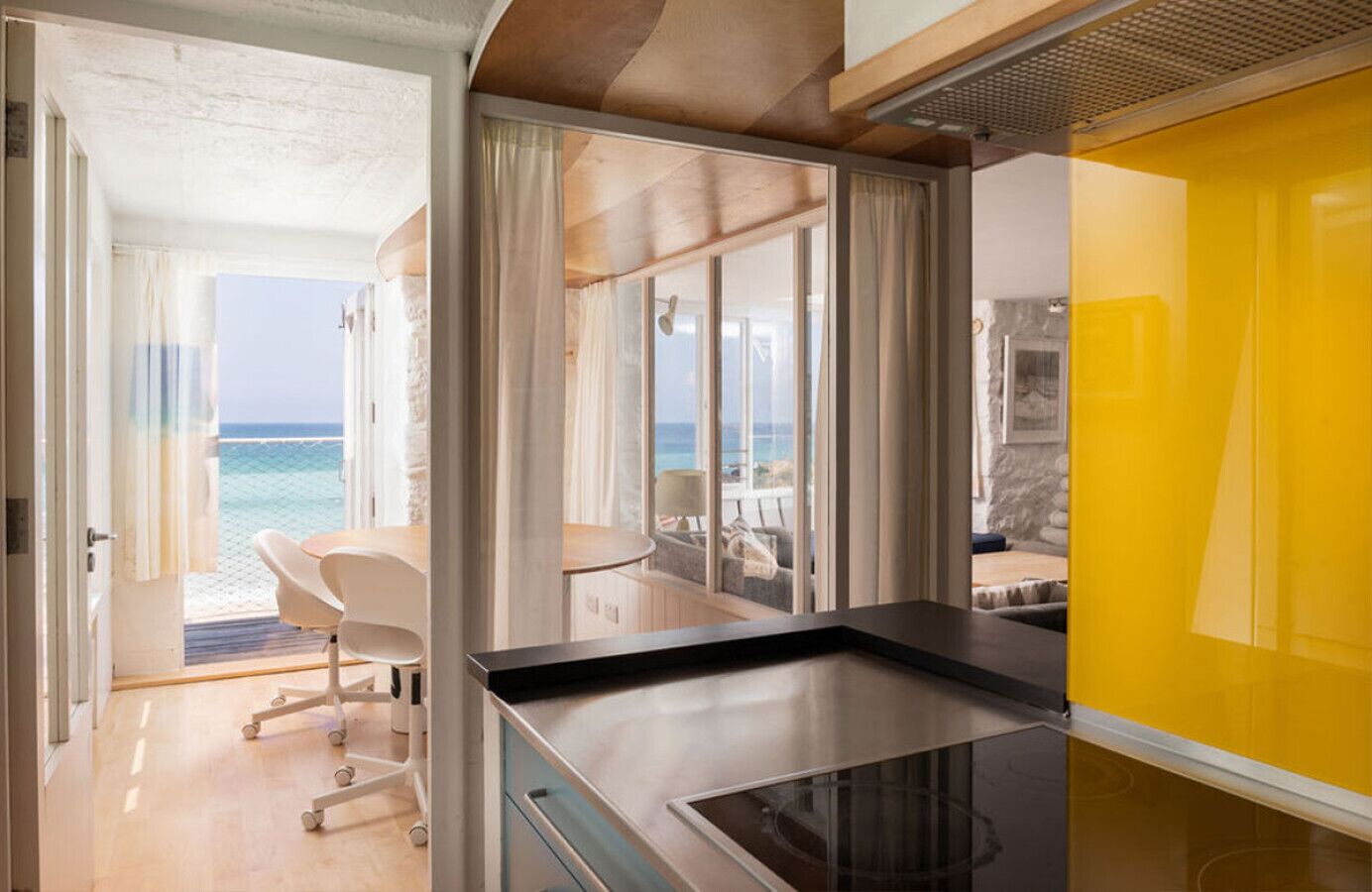 A modern interior with a view of the sea, a dining area, and a yellow accent wall.