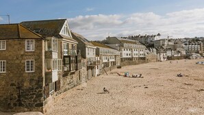 A coastal town with stone buildings, a sandy beach, and a clear sky. - Old Saltings, overlooking Porthmeor beach (St Ives)
