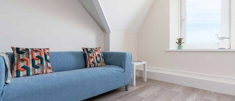 A room with a blue sofa, a small white table, and a window with a view of the sky.
