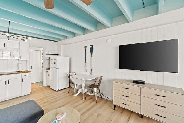 A modern kitchen with white cabinets, a dining area with a white table and chairs, a flat-screen TV mounted on the wall, and a wooden bench.